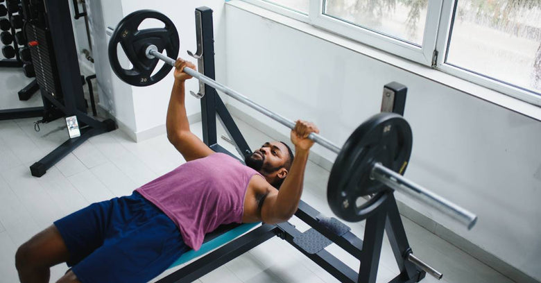 A man, lying on a bench in a home gym, holds on to a barbell as he prepares to lift weights during his workout.