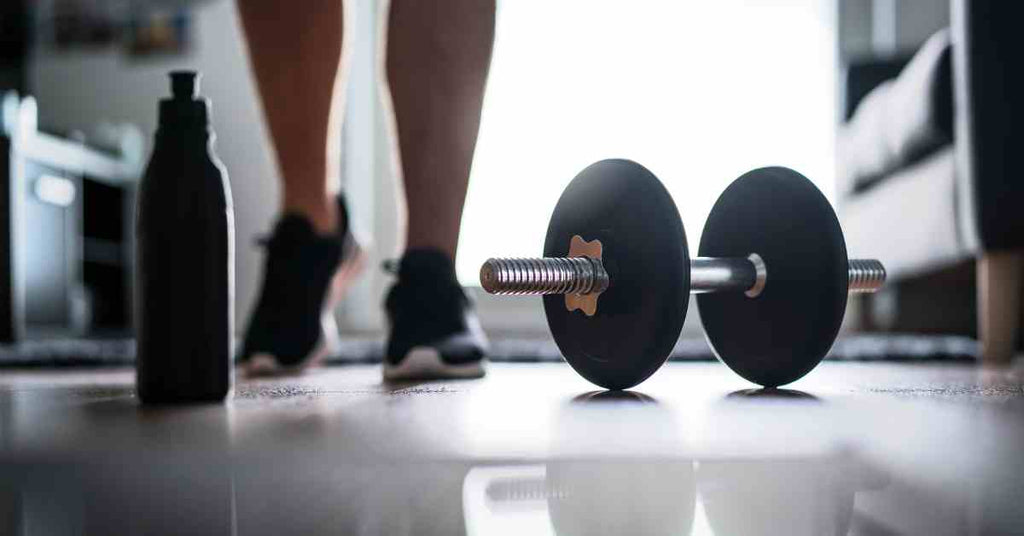 A set of dumbbells sitting on the floor next to a water bottle. A person walks up behind both of the two objects.